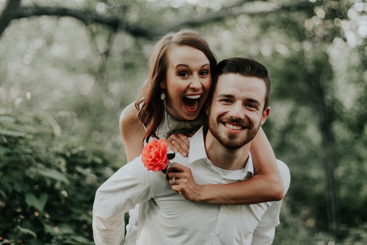 a couple who both have smiles on their face while standing in a forest